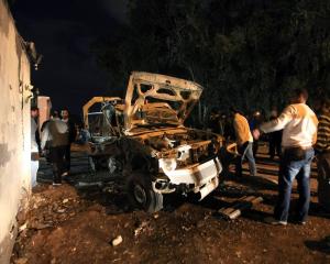 People stand near a police car that was destroyed in an explosion in front of a police station in...