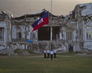 Police lower the national flag in front of the damaged presidential palace on the first...
