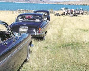The wedding cars wait at the photo stop overlooking Lake Benmore while Joseph Cameron and...