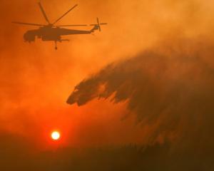 A firefighting helicopter makes water drop as a wildfire burns near the village of Metochi. Photo...