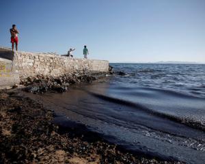 Locals look at a beach covered with oil that leaked from a small oil tanker that sank on...