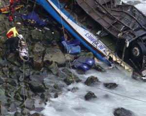 Rescue workers work at the scene after a bus crashed with a truck and careened off a cliff along...