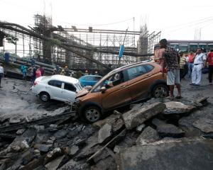 People stand next to the wreckage of vehicles at the site of a bridge that collapsed in Kolkata....