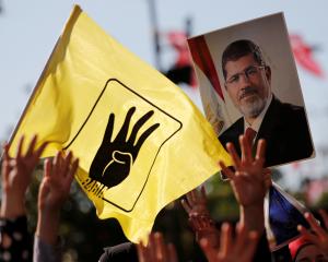 People flash Rabia signs as they hold a picture of former Egyptian president Mursi during a...