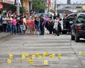 People stand near bullet casings on the ground at a crime scene after a shootout in the...