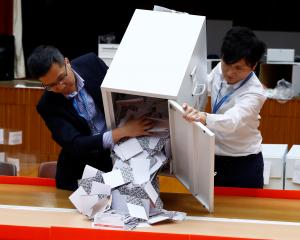 Officials open a ballot box at the polling station in the South Horizons West district as voting...