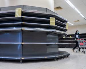 A female shopper in Hong Kong wearing a surgical mask walks past empty supermarket shelves,...