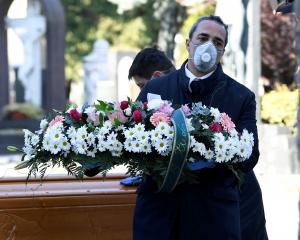 Cemetery workers and funeral agency workers in protective masks transport a coffin of a person...