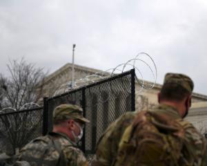 Officers from the National Guard walk near a fence lined with barbed wire at the Capitol grounds...