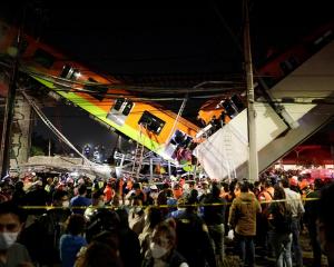 Rescuers work at a site where an overpass for a metro partially collapsed with train cars on it...