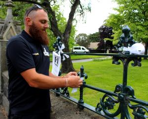 Chris Moore, of Isaac Construction, ties a white ribbon to the fence of First Church of Otago...
