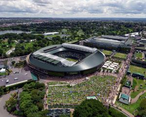 Tennis fans watch a big screen outside Wimbledon's Court 1 with Centre Court in the background....