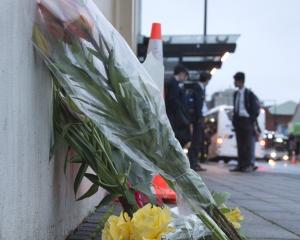 High school pupils wait for their bus yesterday morning beside flowers placed at the scene of...
