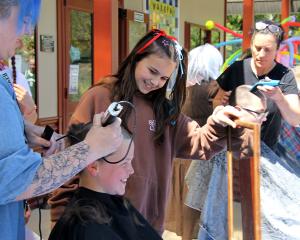 Mala McNab, 12, holds a mirror for Charlie Maze, 13 to watch Ema Soole shave his hair away, while...