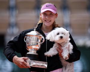 Russia's Mirra Andreeva celebrates with the trophy and a dog after winning her final match...