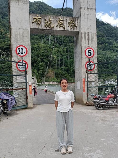 Photo shows Yu Yanqia standing in front of a bridge near her home in the Nujiang Lisu Autonomous...