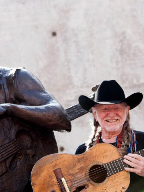 Singer Willie Nelson poses beside a statue of himself during its unveiling in downtown Austin,...