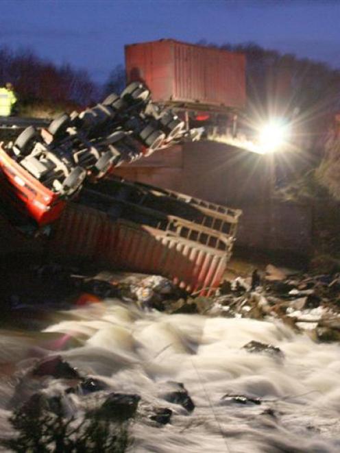 The upside down cab of a truck and trailer unit hangs over the side of a bridge near Browns, in...