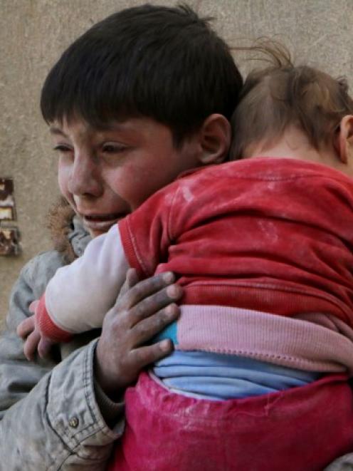 A boy holds his baby sister saved from under rubble, who survived what activists say was an...