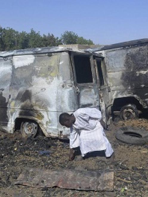 A boy searches the ground next to a burnt-out vehicle, caused by an attack from Boko Haram...