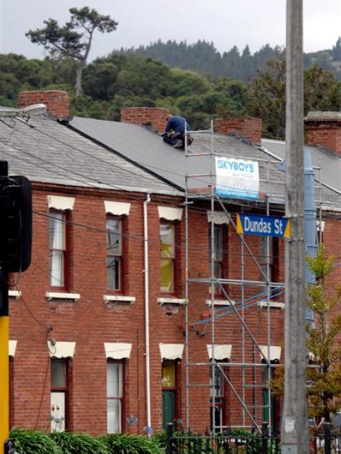 A building contractor replaces a slate tile roof with corrugated iron on one of the historic...