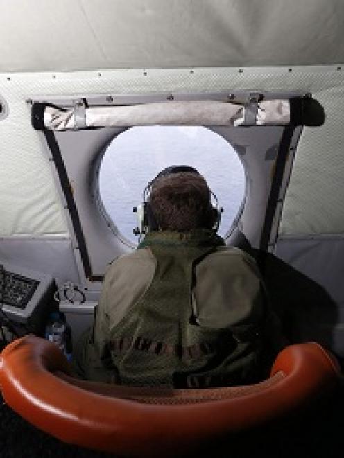 A crewman aboard a Royal New Zealand Air Force P-3K2 Orion aircraft scans the ocean for missing...