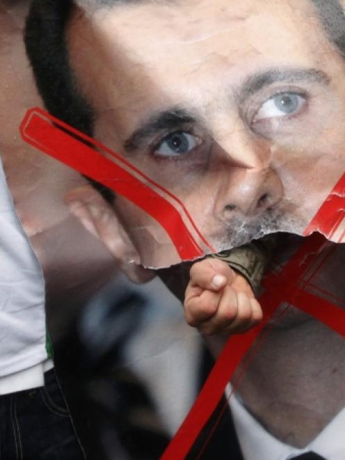A demonstrator punches through a portrait of Syria's President Bashar al-Assad during a protest...