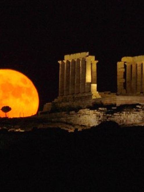 A full moon rises behind the ancient temple of Posseidon, in Sounio about 73km southeast of...
