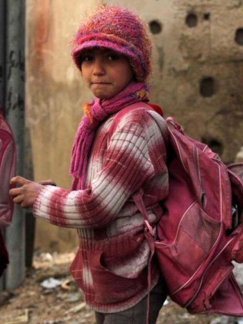 A girl carries a torn school bag as she stands in front of debris outside a school in the Duma...
