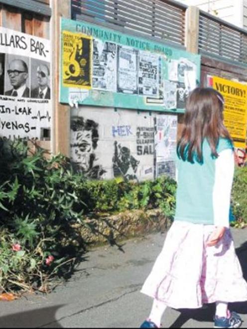 A girl walks past a fence full of posters and notices. Image created by graphic artist Alistair...