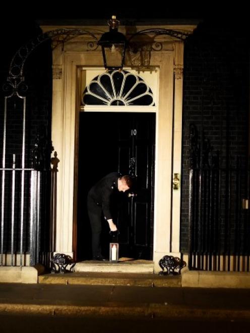 A guard places a lantern at the front door of Number 10 Downing St during 'Lights Out', as part...
