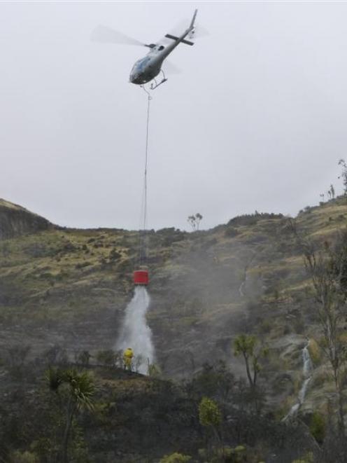 A helicopter dumps water on a site at the base of Cecil Peak  the day after the fire last year....
