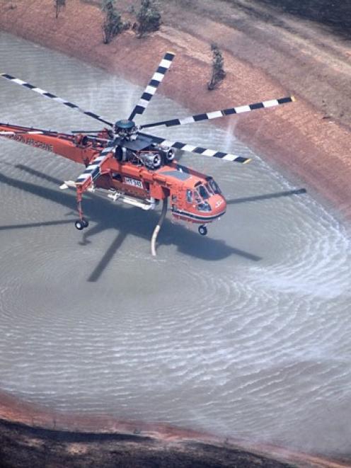 A helicopter sucks up water from a small dam to drop on a bushfire burning in the Grampians...
