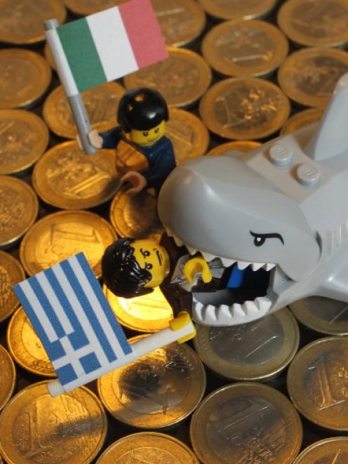 A Lego shark chomps down on a Lego figure holding a Greek flag as another figure holding an...