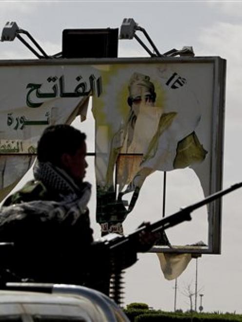A Libyan volunteer stands guard near a defaced billboard of Libyan leader Moammar Gadhafi in the...