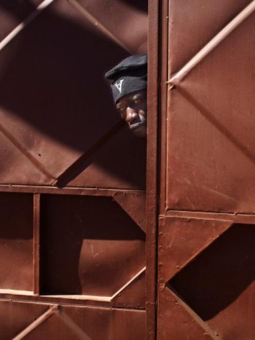 A Malian soldier peeks through a doorway behind which Malian and French soldiers are stationed in...