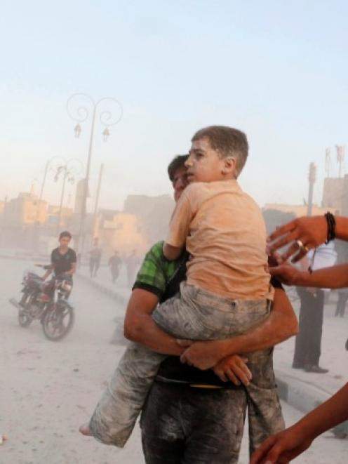 A man carries an injured child at a damaged site hit by what activists said were two barrel bombs...