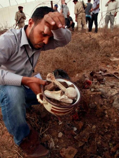 A man collects human remains at the site of a mass grave in Tripoli said by authorites to contain...