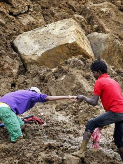 A man helps another make his way through deep mud at the site of a landslide at the Koslanda tea...