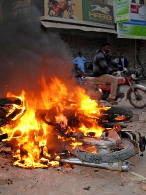 A man rides past motorbikes being burnt by supporters of Pakistan People's Party in Larkana to...