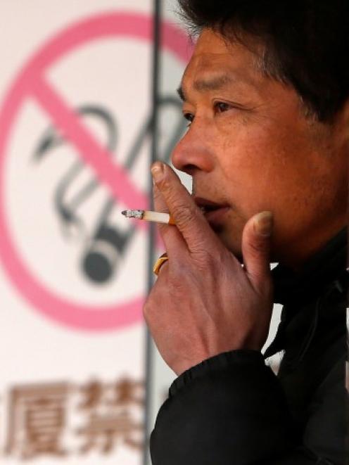A man smokes in front of a 'no smoking' sign outside a shopping mall in Shanghai. REUTERS/Aly...