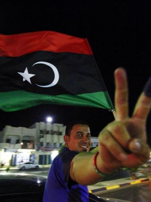 A man, with an inked finger, flashes the victory sign as he celebrates with the new Libyan flag...