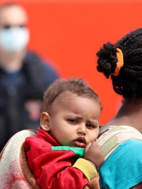 A migrant carries her baby on her shoulders aboard a navy ship before being disembarked in the...
