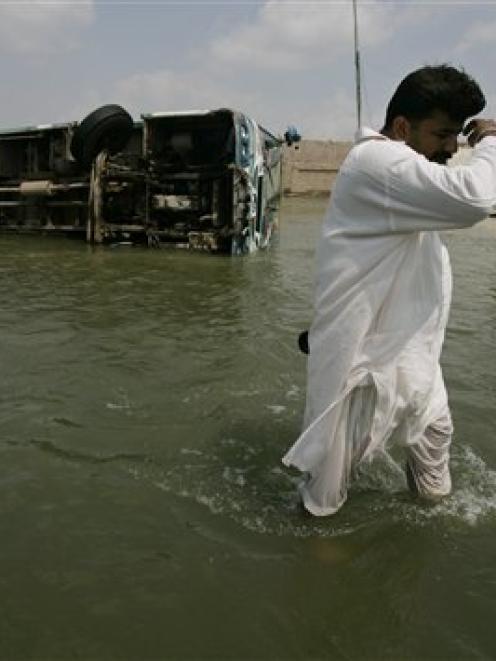 A Pakistani man passes by a toppled passenger bus along a flooded street in Muzaffargarh, Punjab...