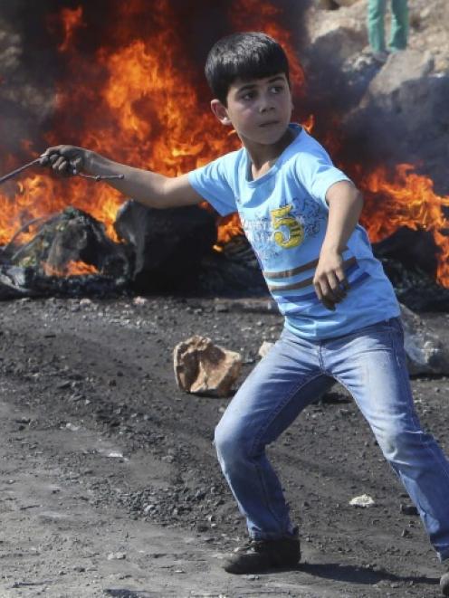 A Palestinian boy uses a sling to throw stones towards Israeli soldiers during clashes following...