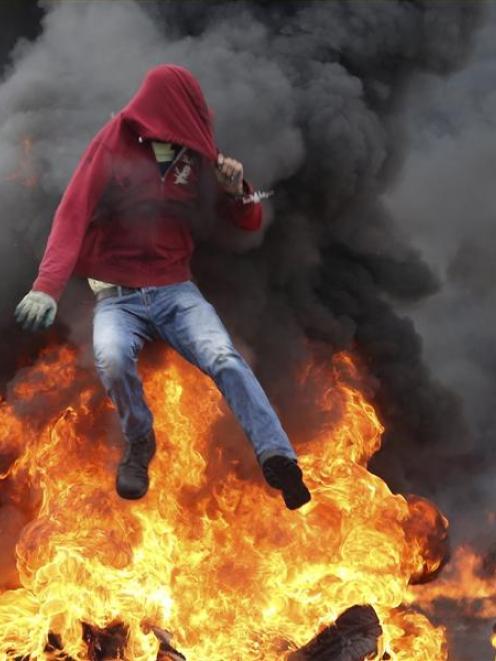 A Palestinian protester jumps over burning tyres during clashes with Israeli troops near the...