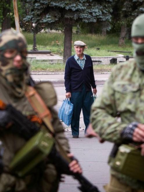 A passer-by stops to look at armed pro-Russian separatists at a town centre in Snizhnye in...