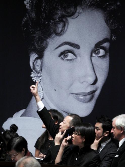 A phone bidder signals his bid near an image of Elizabeth Taylor during an auction of the late...