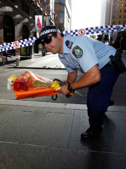 A police officer carries a bouquet under cordon tape as floral tributes are relocated after the...