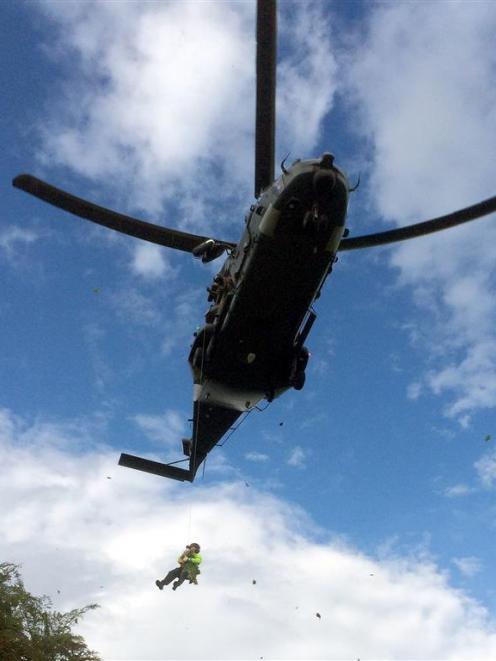 A police officer  hangs beneath an RNZAF NH90 during a cannabis recovery operation over Westwood...